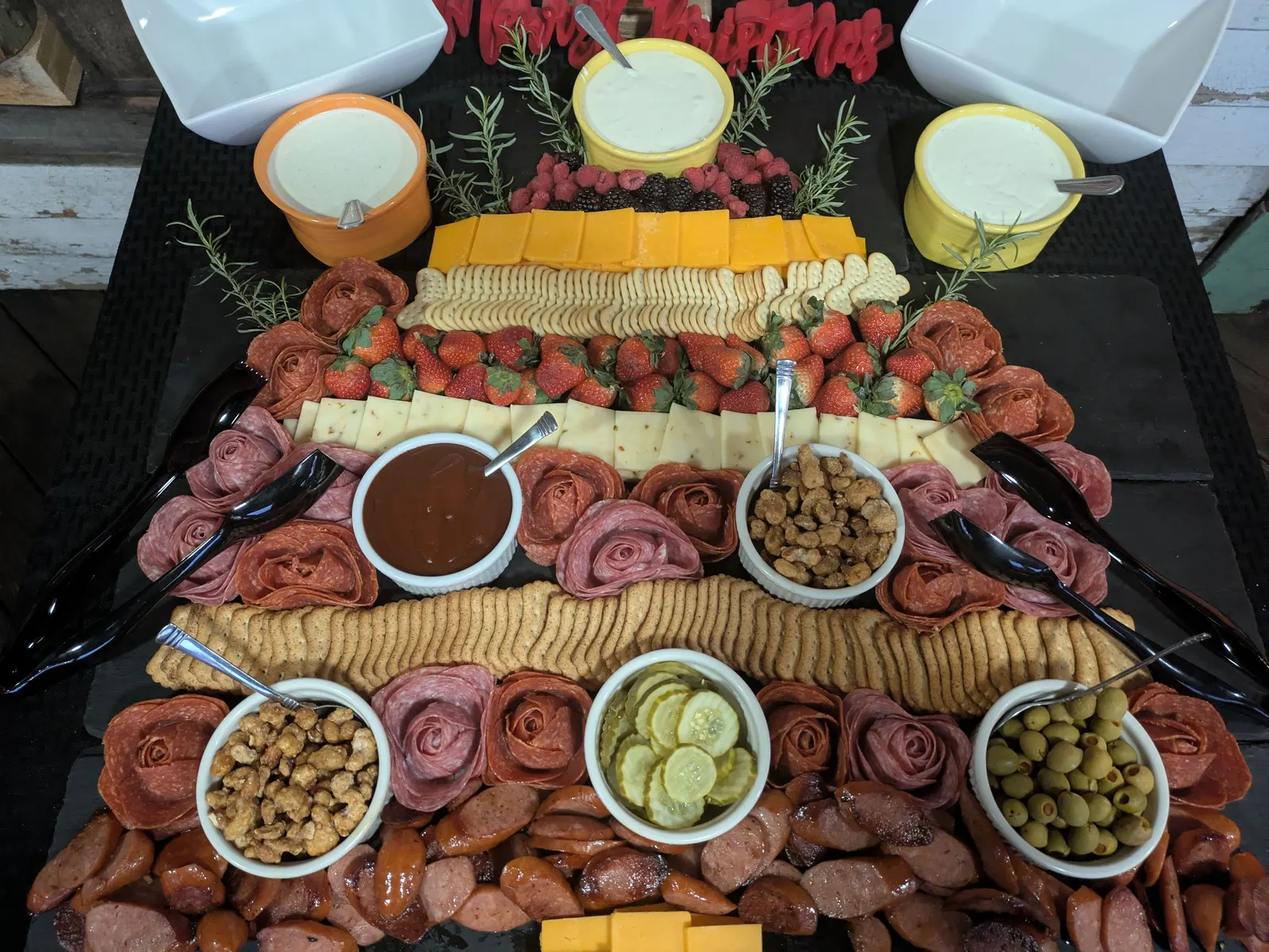 A Christmas tree-shaped charcuterie board of salami roses, cheeses, crackers, strawberries, pickles and olives