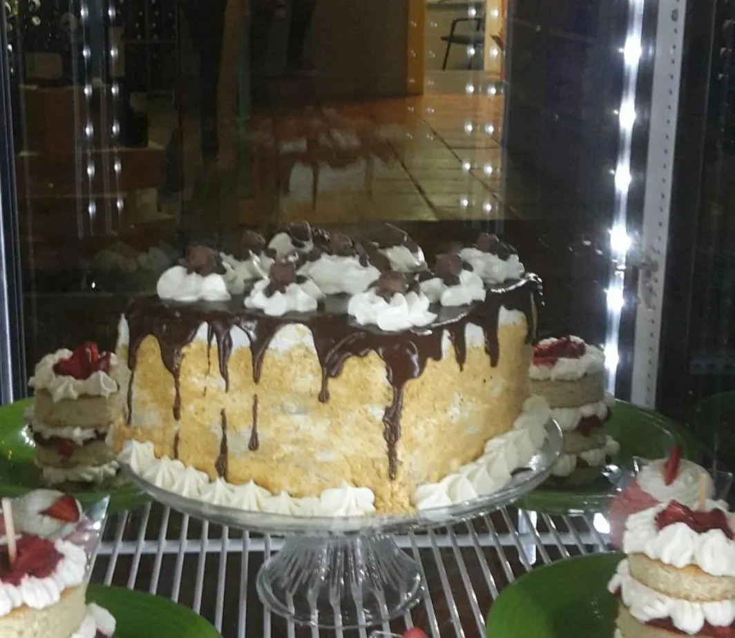 A cake with a chocolate drip and whipped cream rosettes in the dessert case