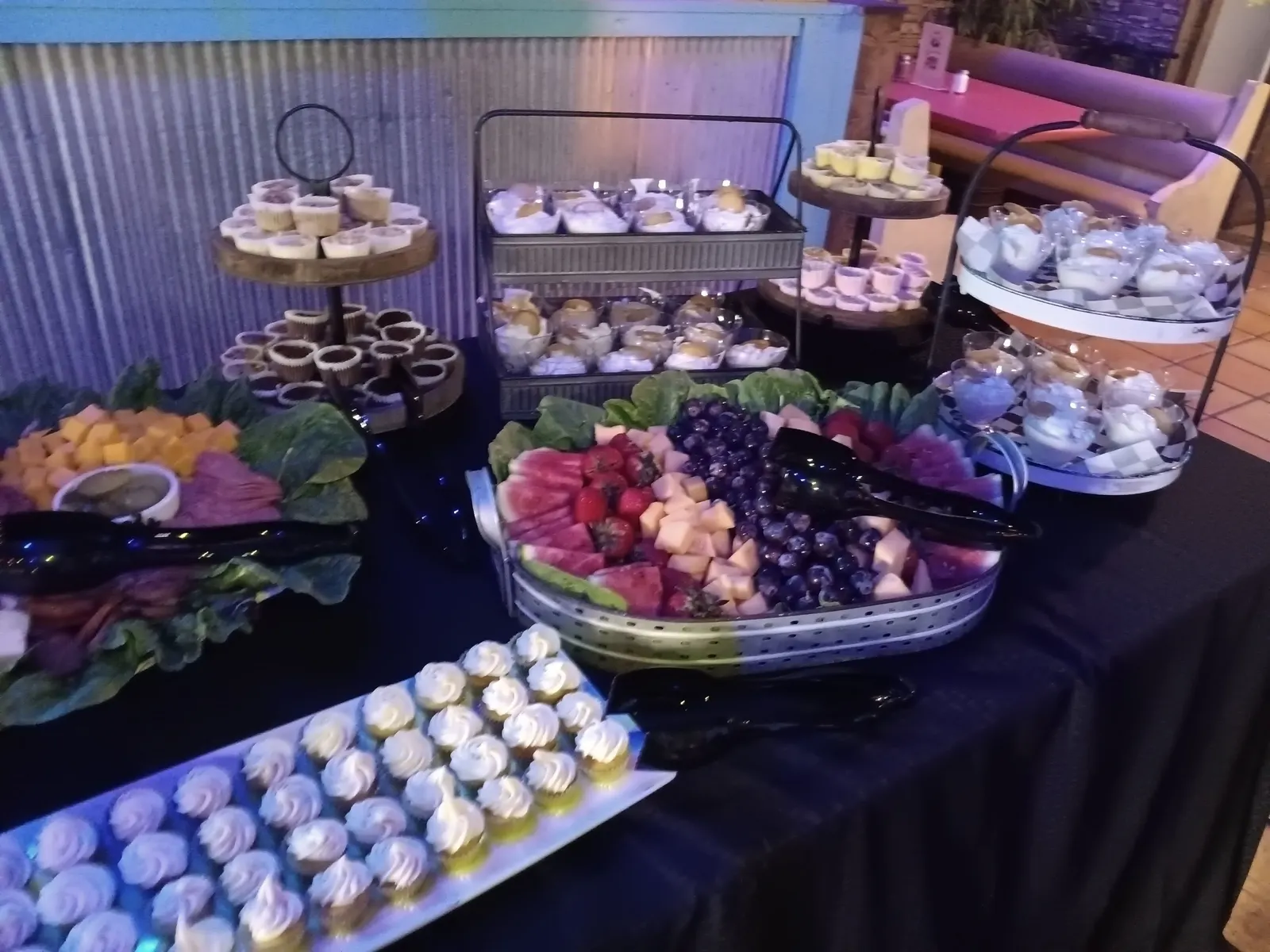 A dessert table with mini cheesecakes, cupcakes, banana pudding cups and a fruit tray