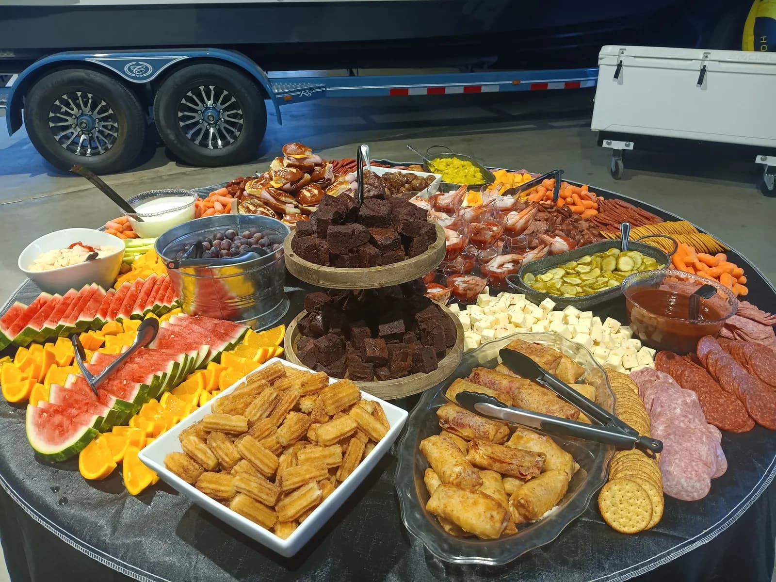 A grazing table with watermelon, oranges, brownies, egg rolls, churros, cheese and crackers