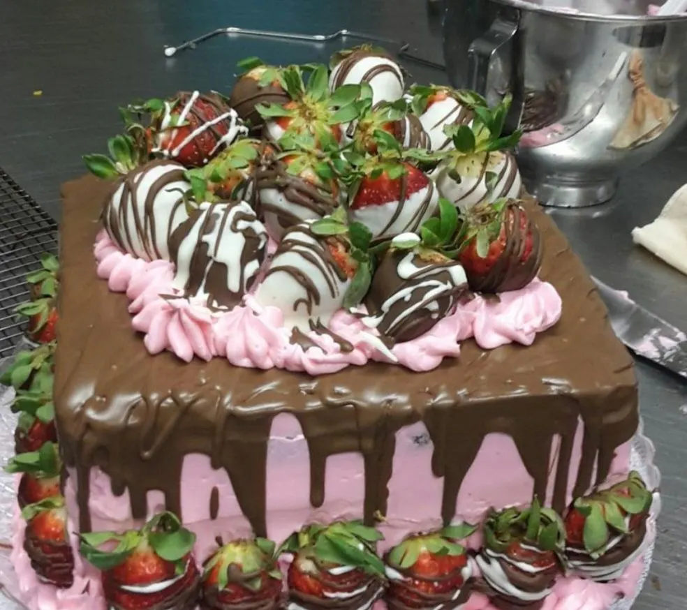 A pink cake with a chocolate drip, topped with chocolate-dipped strawberries