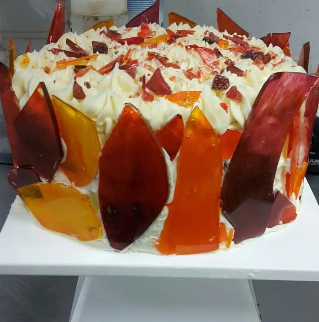 A white frosted cake ringed with shards of red and orange sugar glass
