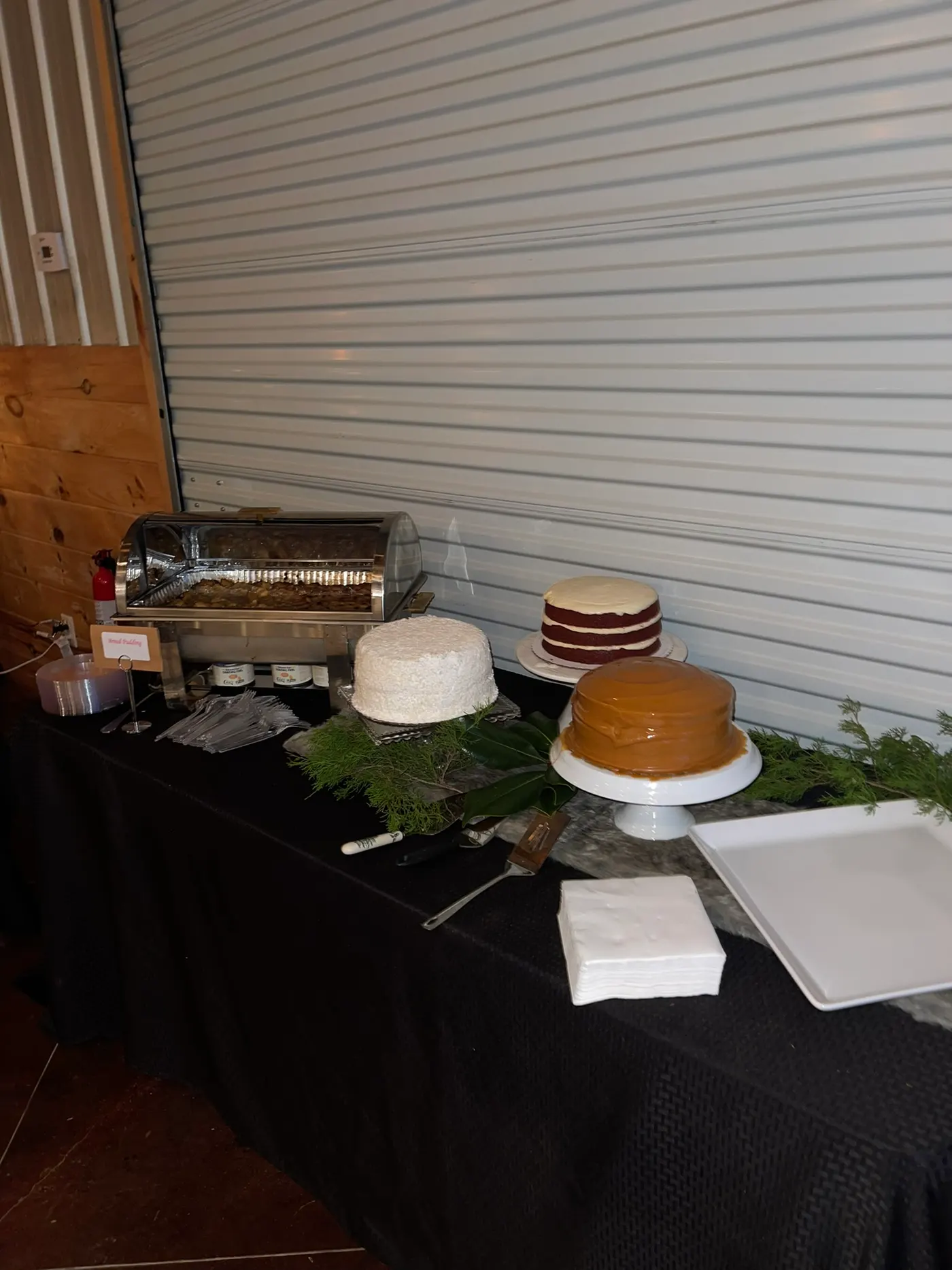 Layer cakes on stands at the end of a buffet, beside a warming tray