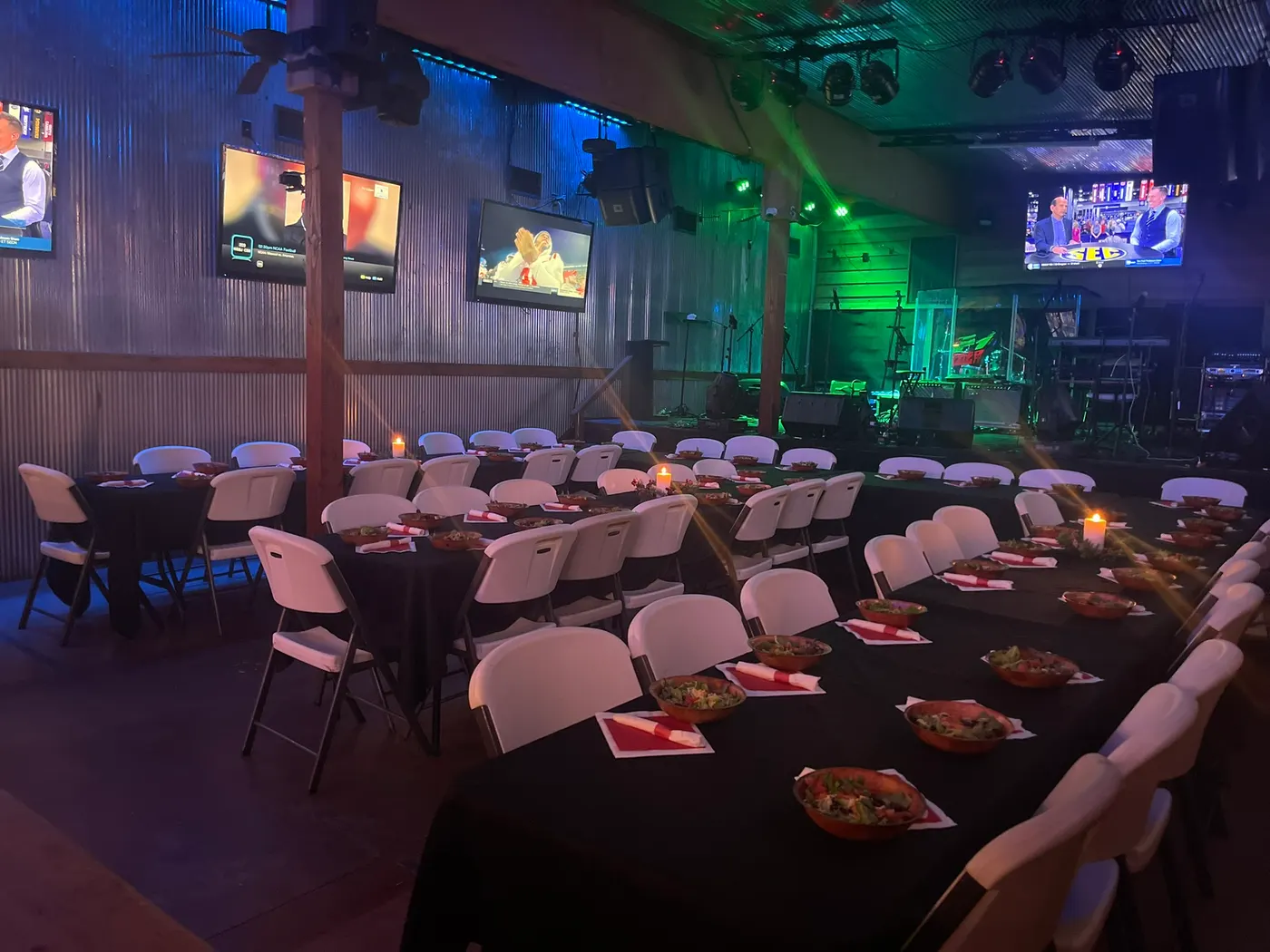 Round and long tables laid out together for a large party, under the wall of TVs